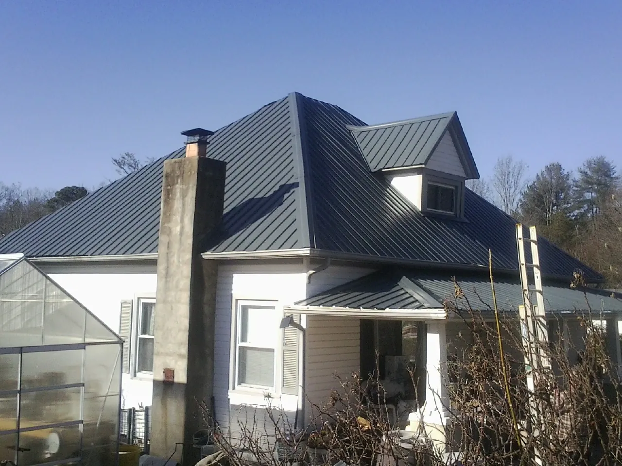 Dark blue standing seam metal roof on a white farmhouse with dormer — Slate & Tile Roof Repair by Roofing Brothers in Waskom