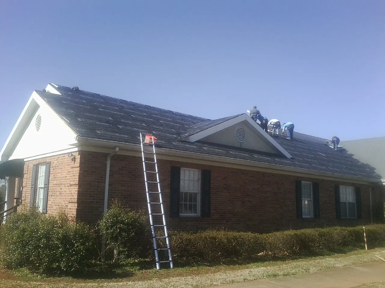 Crew tearing shingles off a brick ranch roof with a ladder set — Metal Roof Repair work by our crew in Waskom