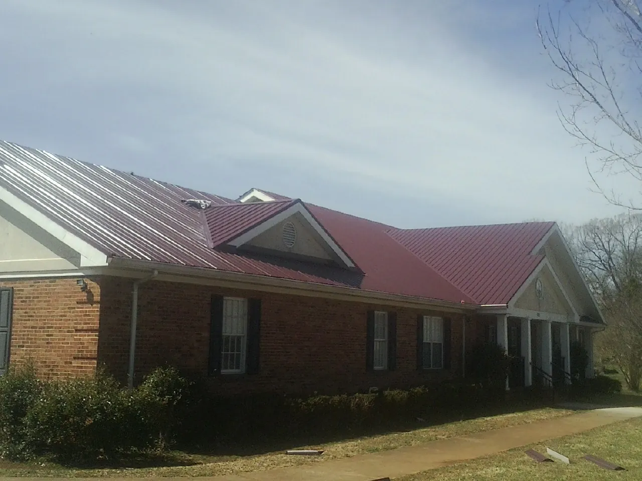 Red metal roof with gabled entries on a long brick building, from a Hail Damage Roof Repair job in Waskom