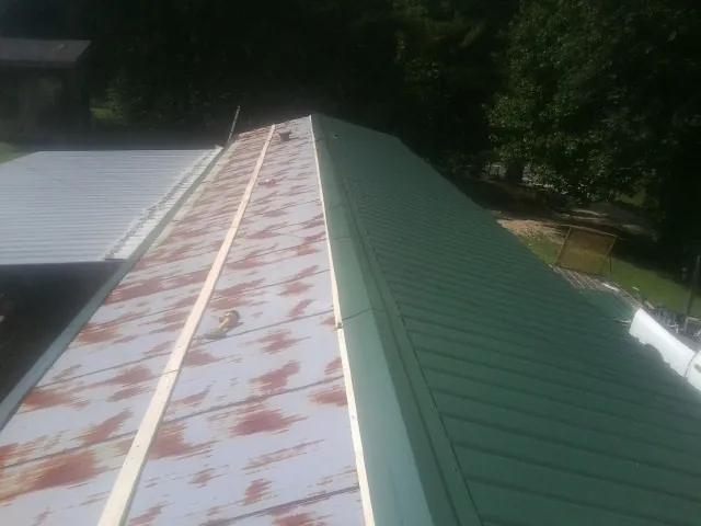 Old rusted panels beside newly installed green metal roofing — Wind Damage Roof Repair by Roofing Brothers in Waskom