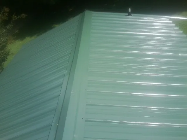 New green metal panels meeting at the ridge of a roof — Flat Roof Repair work by our crew in Waskom