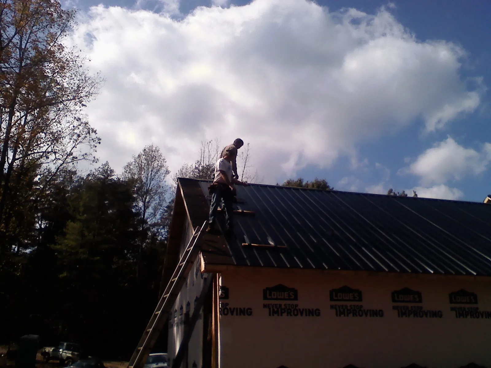 Roofer fastening dark metal panels high against a cloudy sky, from a Roof Inspection job in Waskom